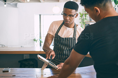 Buy stock photo Shot of a young man using a digital tablet while buying coffee in a cafe