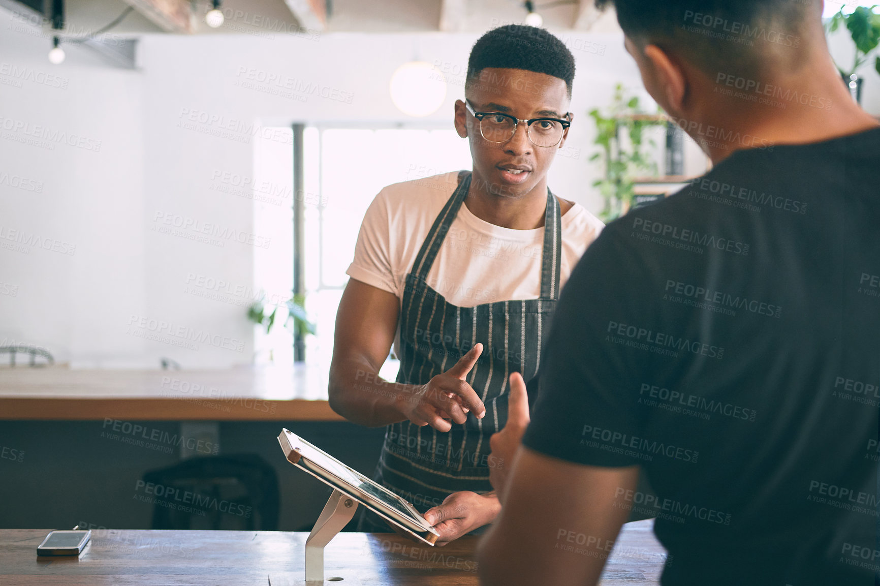 Buy stock photo Shot of a young man using a digital tablet while buying coffee in a cafe