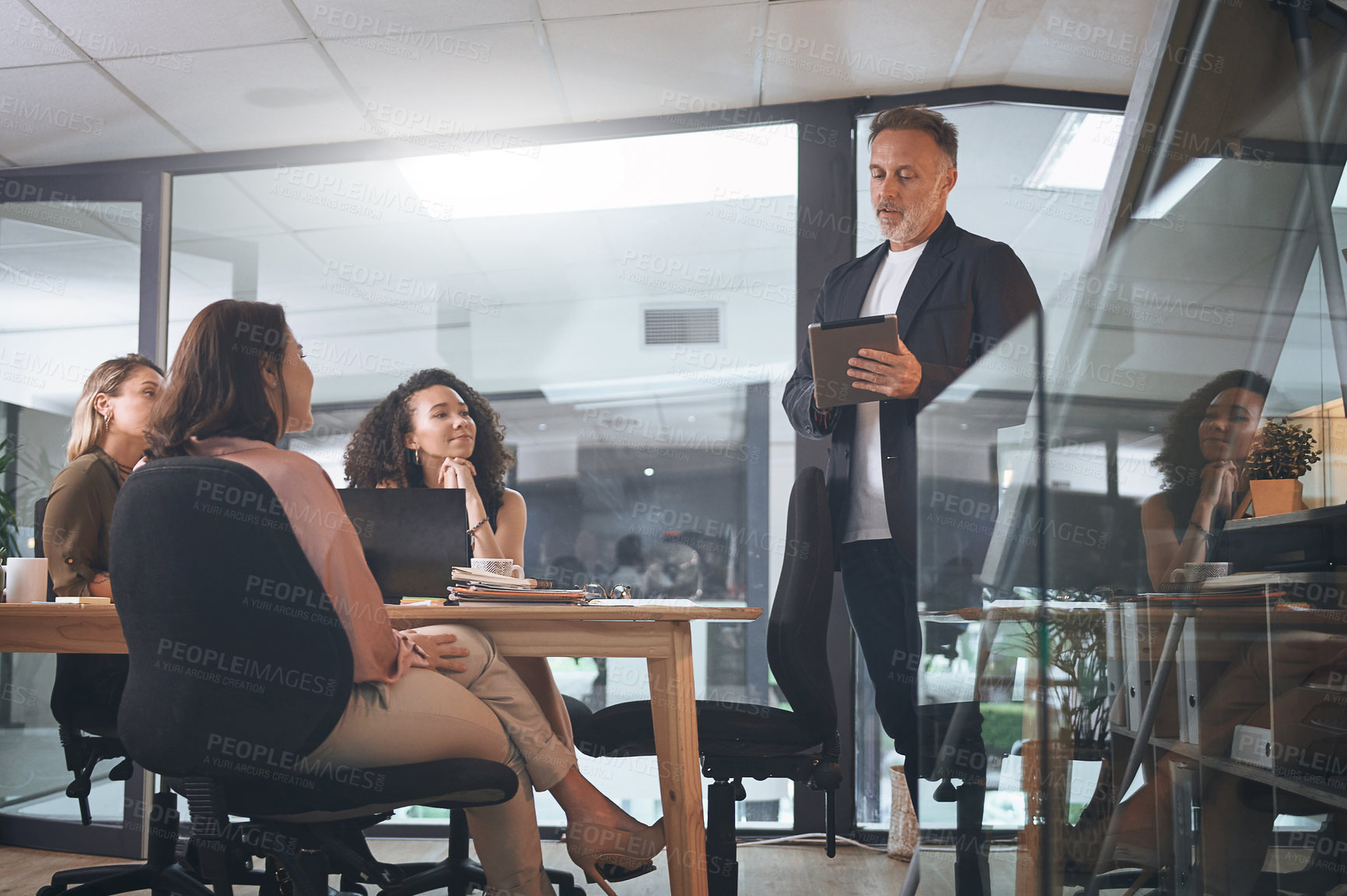 Buy stock photo Shot of a mature businessman using a digital tablet while delivering a presentation in the boardroom of a modern office