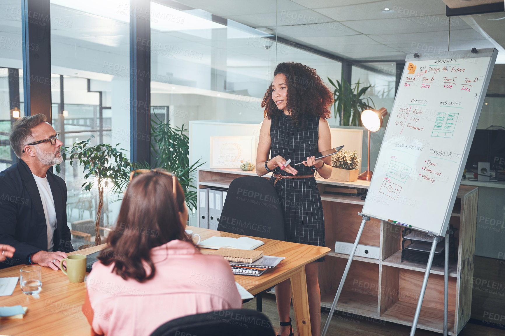 Buy stock photo Shot of a young businesswoman using a digital tablet delivering a presentation to her coworkers in a modern office