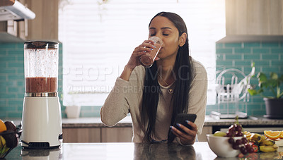 Buy stock photo Smoothie, phone and woman in kitchen for breakfast, texting and healthy diet in her home. Fruit, shake and female health influencer with smartphone app for social media, blog or vlog for vegan recipe