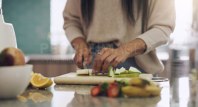 Buy stock photo Shot of an unrecognizable woman cutting fruit to prepare a smoothie on her kitchen at home