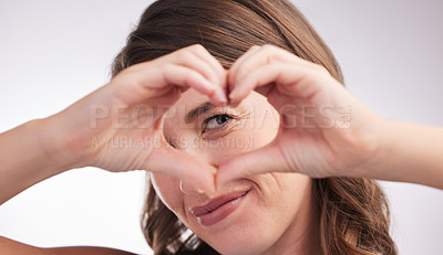 Buy stock photo Studio portrait of a young woman making a heart shape with her hands against a grey background