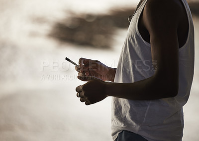 Buy stock photo Shot of an unrecognisable man smoking a marijuana cigarette against an urban background