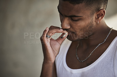 Buy stock photo Shot of a young man smoking a marijuana cigarette against an urban background