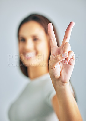 Buy stock photo Studio shot of a young woman showing the peace sign against a grey background.