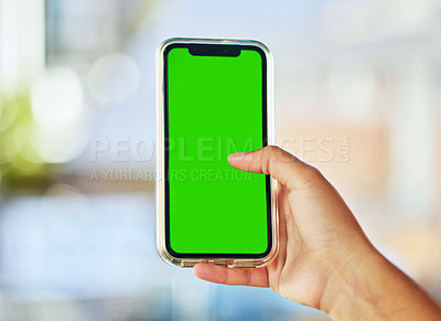 Buy stock photo A young woman holding up a smartphone with a green screen against a defocused background.