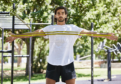 Buy stock photo Shot of a young man using his resistance band outside in the park