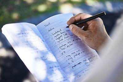 Buy stock photo Shot of a unrecognizable man writing in his notebook outside in the park