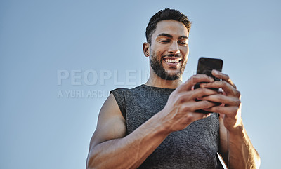 Buy stock photo Low angle shot of a sporty young man using a cellphone while exercising outdoors