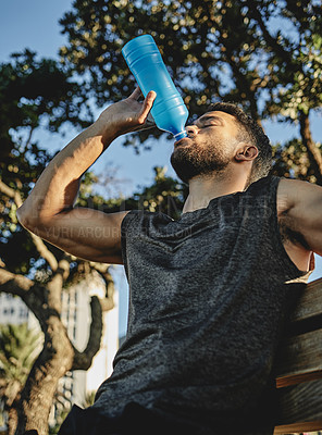 Buy stock photo Low angle shot of a sporty young man drinking water while exercising outdoors