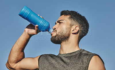 Buy stock photo Low angle shot of a sporty young man drinking water while exercising outdoors