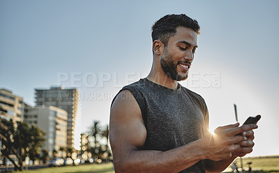 Buy stock photo Shot of a sporty young man using a cellphone while exercising outdoors