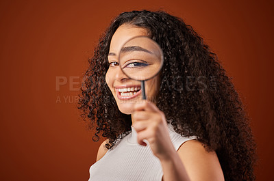 Buy stock photo Cropped portrait of an attractive young woman looking through a magnifying glass in studio against a red background