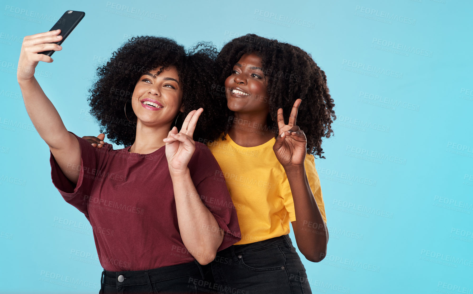 Buy stock photo Studio shot of two young women using a smartphone to take selfies against a blue background