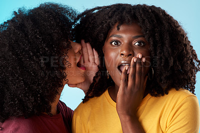 Buy stock photo Studio shot of a young woman whispering in her friend’s ear against a blue background