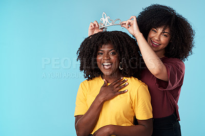 Buy stock photo Studio shot of a young woman putting a crown on her friend against a blue background