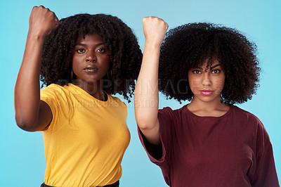 Buy stock photo Studio shot of two young women raising their fists in solidarity against a blue background