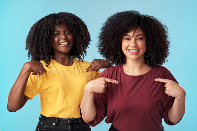 Buy stock photo Studio shot of two young women pointing at their t shirts against a blue background