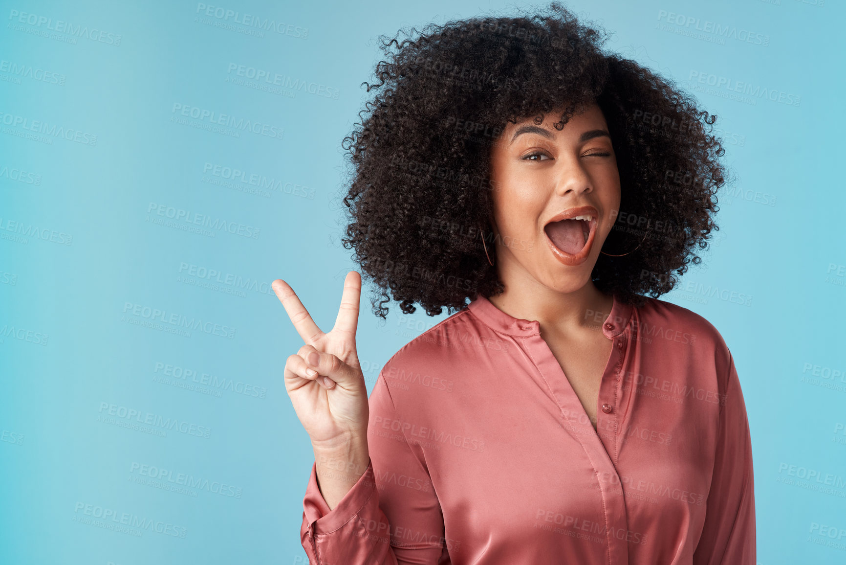 Buy stock photo Studio shot of an attractive young woman making a peace gesture against a blue background