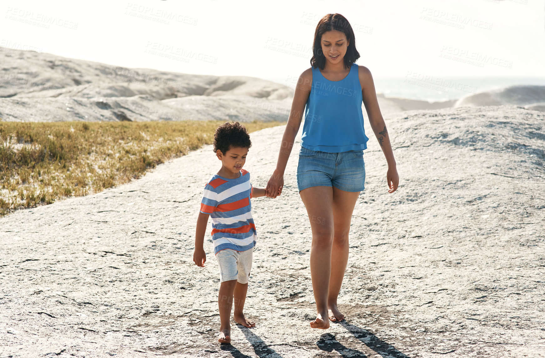 Buy stock photo Shot of a mother taking a stroll on the beach with her son