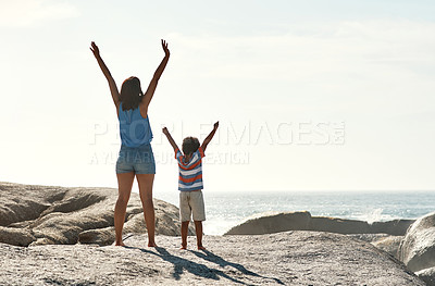 Buy stock photo Shot of a parent with their child raising their arms in the sunlight at the beach