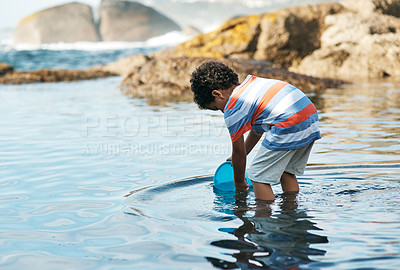 Buy stock photo Shot of a young boy playing in the water at the beach using a bucket to catch things
