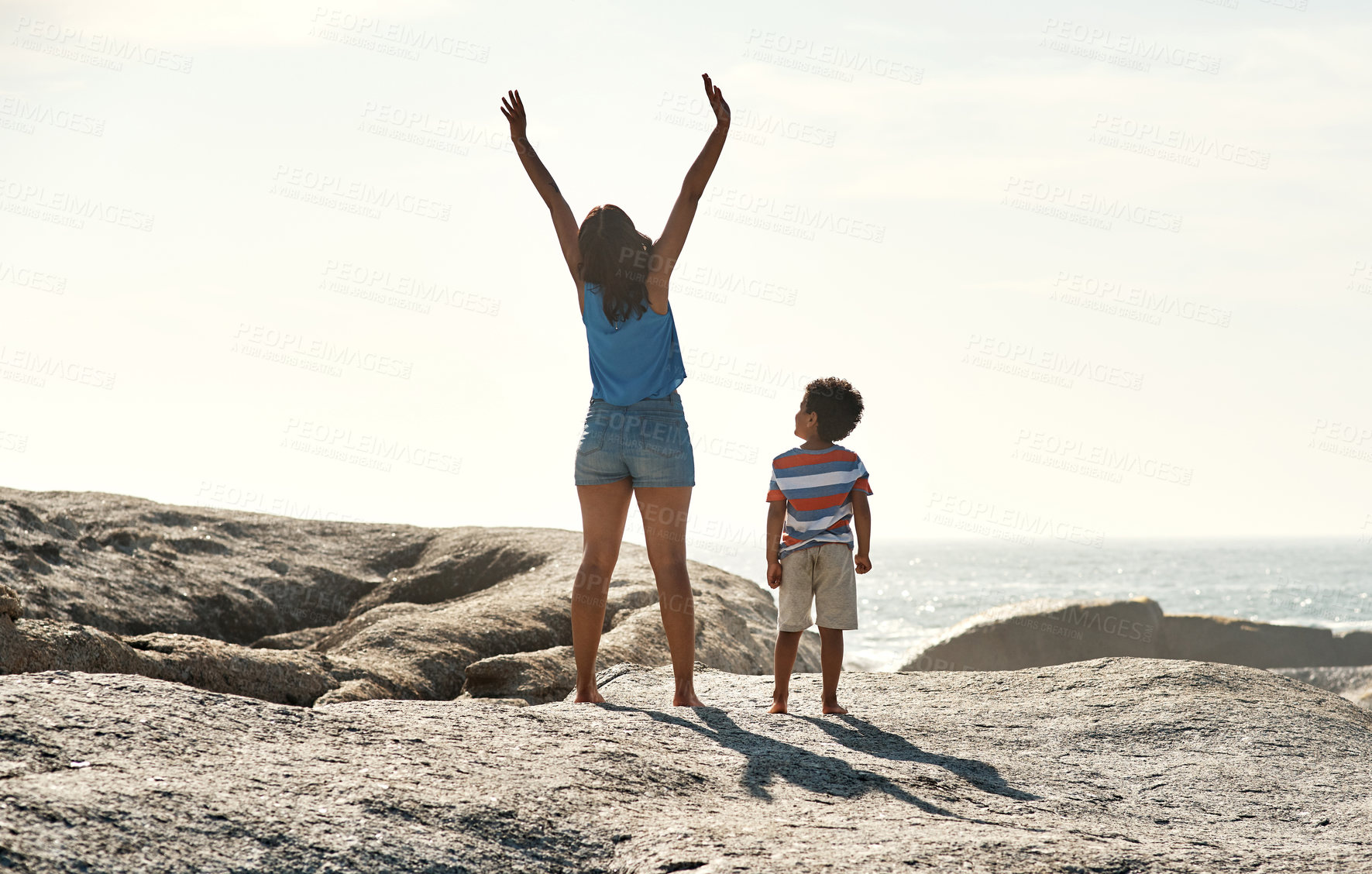 Buy stock photo Shot of a parent with their child raising their arms in the sunlight at the beach