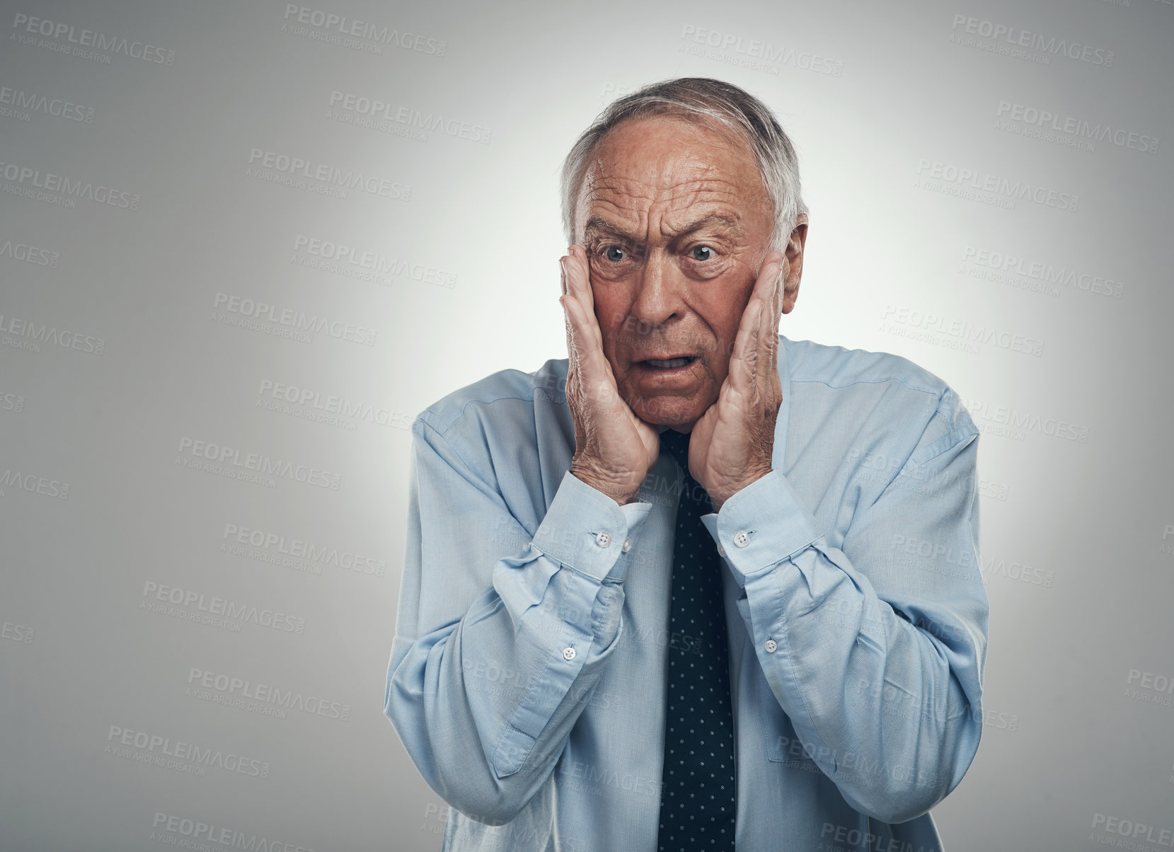 Buy stock photo Shot of a senior businessman standing against a grey studio background with his face in his hands and looking shocked