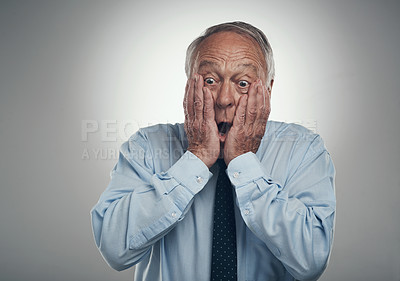 Buy stock photo Shot of a senior businessman standing against a grey studio background with his face in his hands and looking shocked