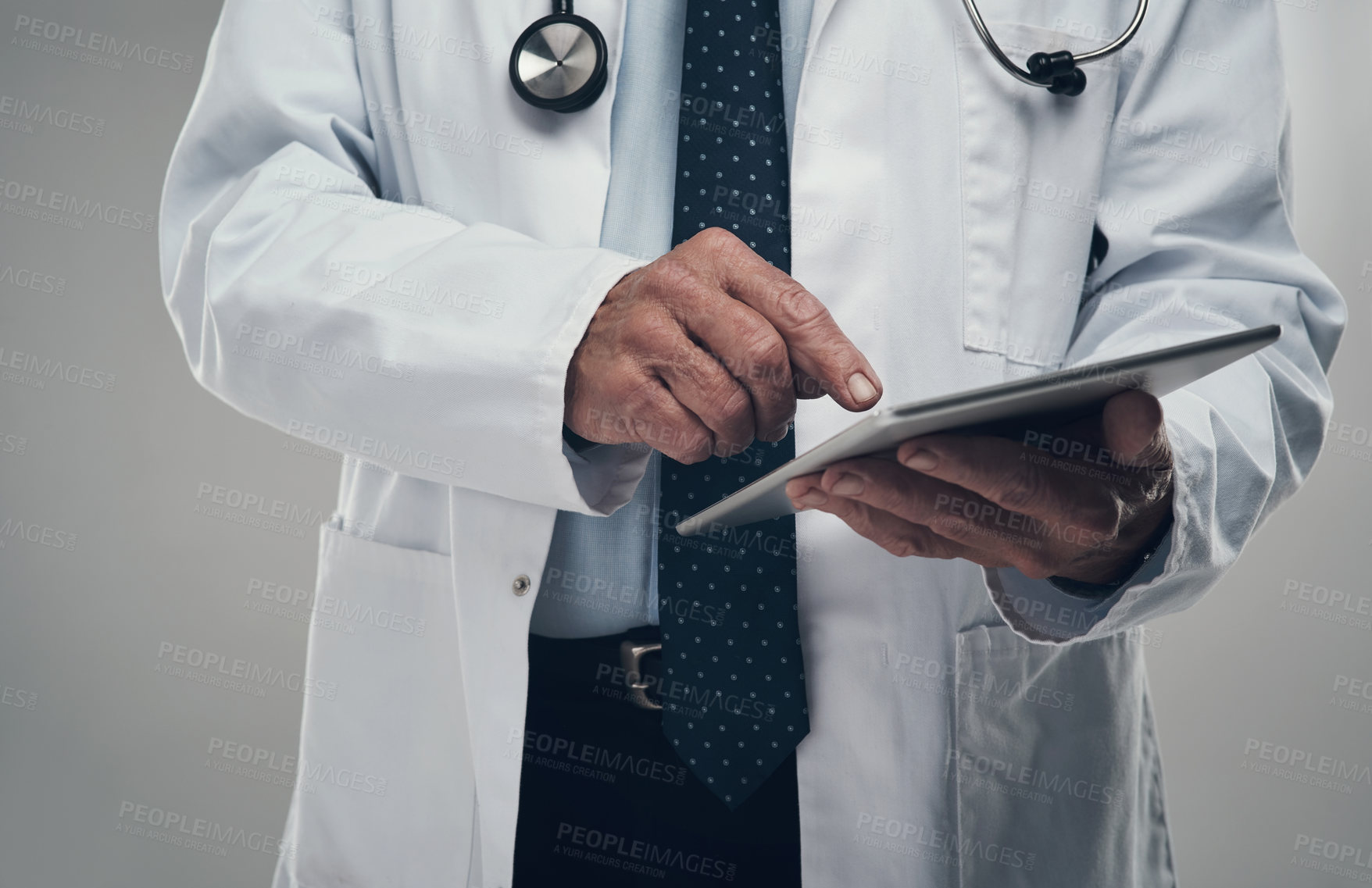 Buy stock photo Shot of an elderly male doctor using a digital tablet in a studio against a grey background