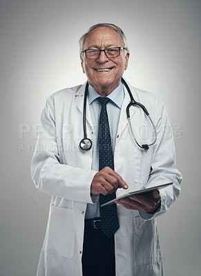Buy stock photo Shot of an elderly male doctor using a digital tablet in a studio against a grey background