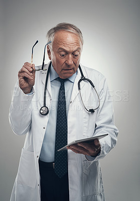 Buy stock photo Shot of an elderly male doctor using a digital tablet in a studio against a grey background