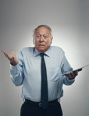 Buy stock photo Shot of a senior businessman standing alone against a grey studio background and looking confused while holding a digital tablet