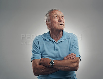 Buy stock photo Shot of an older man with his arms crossed looking off into the distance in a studio against a grey background