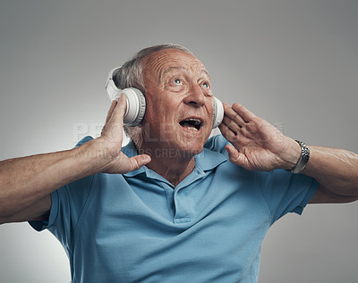 Buy stock photo Shot of an elderly male wearing headphones and listening to music in a studio against a grey background