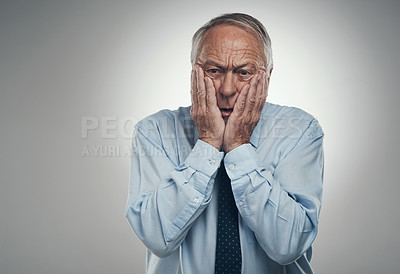Buy stock photo Shot of a senior businessman standing against a grey studio background with his face in his hands and looking concerned