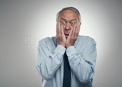 Buy stock photo Shot of a senior businessman standing against a grey studio background with his head in his hands and looking scared