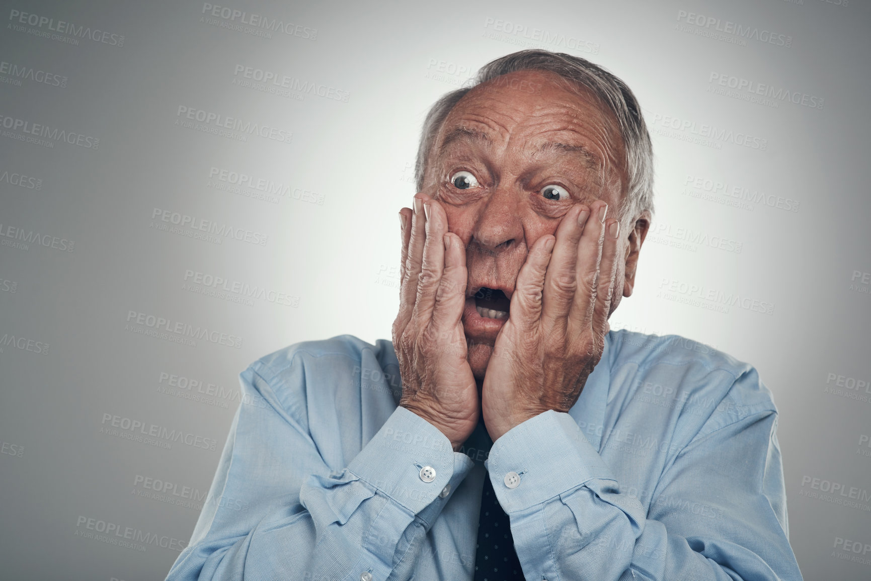 Buy stock photo Shot of a senior businessman standing against a grey studio background with his face in his hands and looking shocked