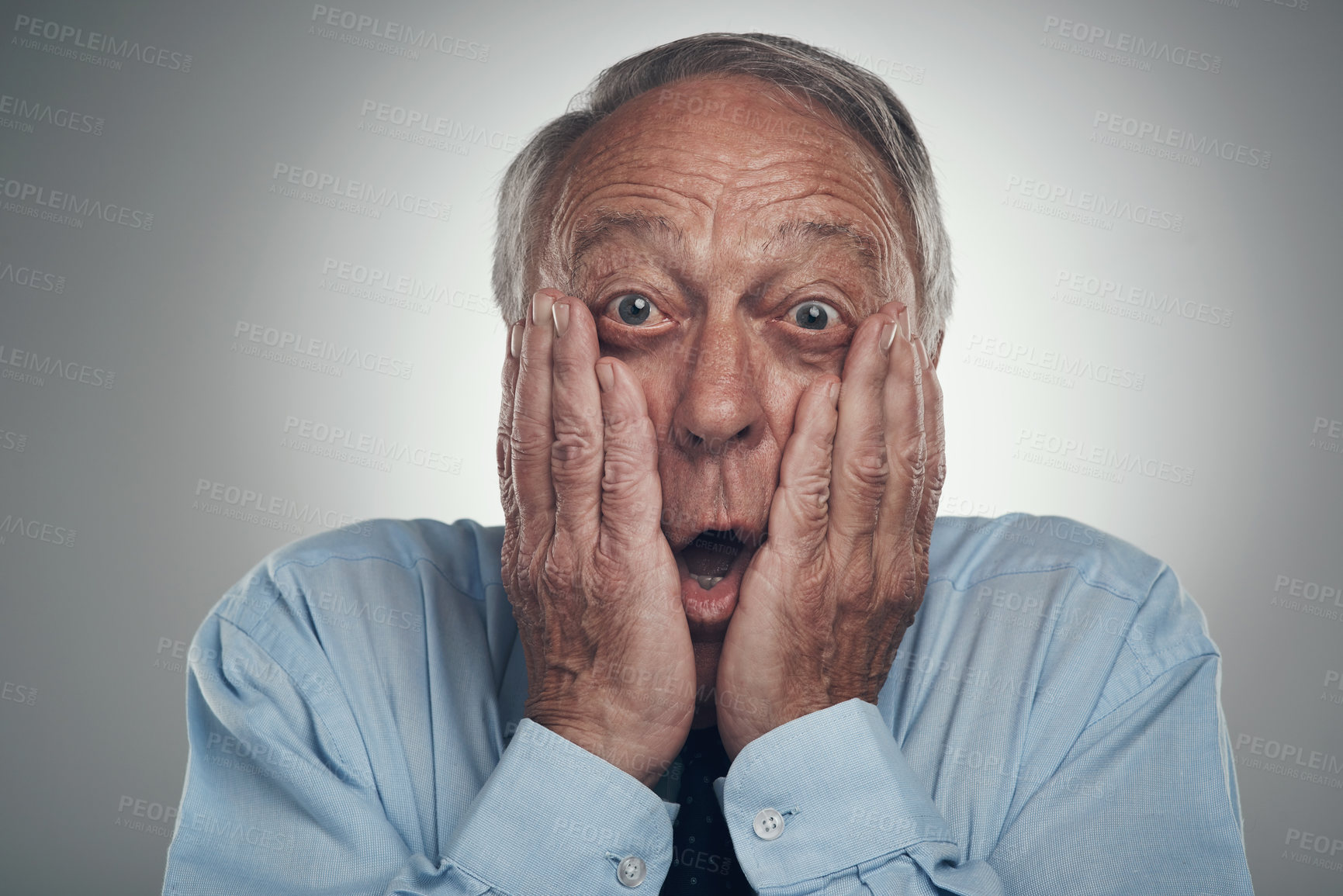 Buy stock photo Shot of a senior businessman standing against a grey studio background with his face in his hands and looking shocked