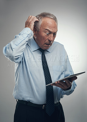 Buy stock photo Shot of a senior businessman standing alone against a grey studio background and looking confused while using a digital tablet