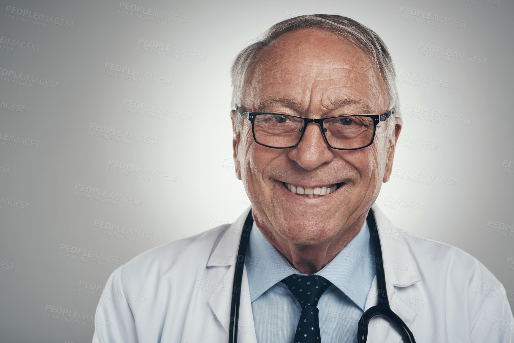 Buy stock photo Shot of a happy elderly male doctor in the studio against a grey background