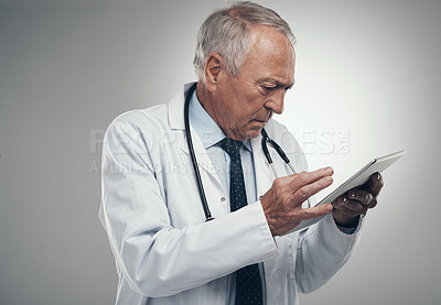 Buy stock photo Shot of an elderly doctor using a digital tablet in a studio against a grey background