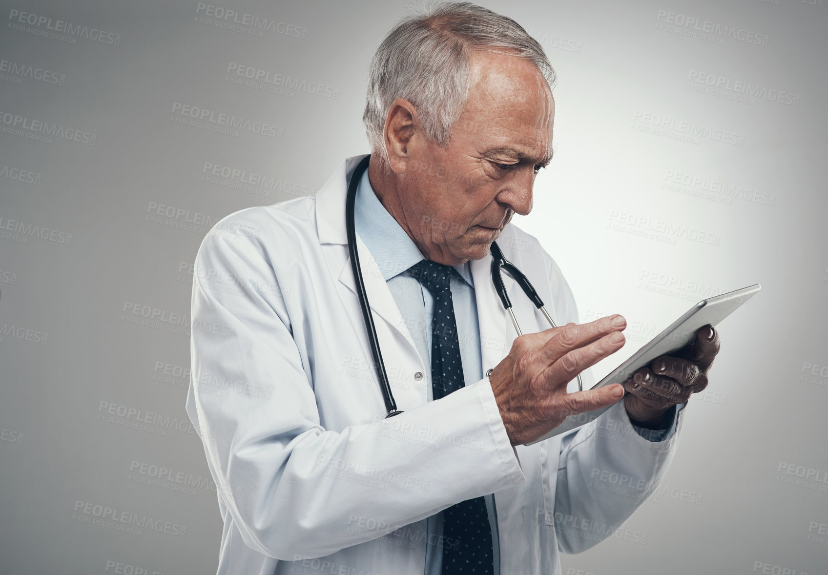 Buy stock photo Shot of an elderly doctor using a digital tablet in a studio against a grey background