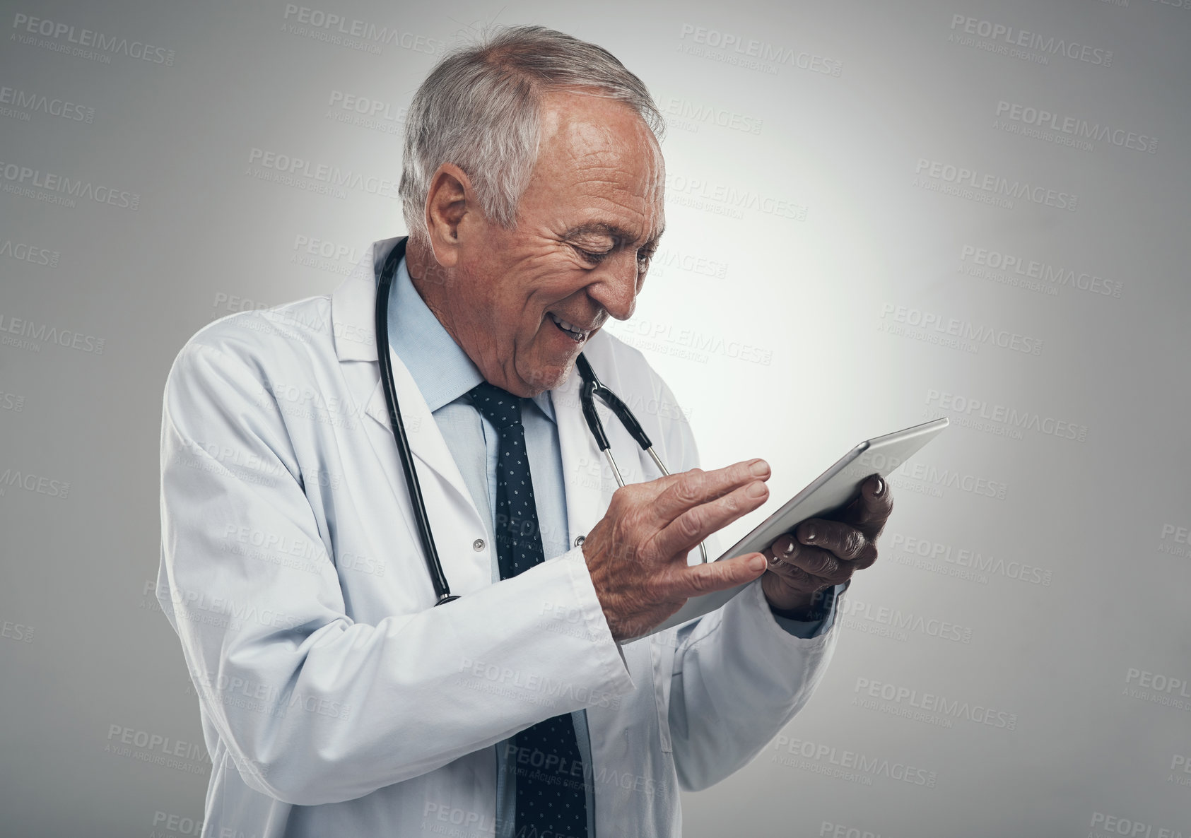 Buy stock photo Shot of an elderly doctor using a digital tablet in a studio against a grey background