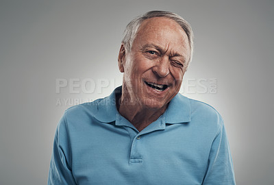 Buy stock photo Shot of a older man winking at the camera in a studio against a grey background
