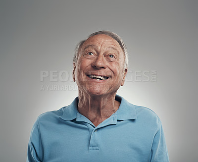 Buy stock photo Shot of an elderly man smiling while gazing above himself in a studio against a grey background