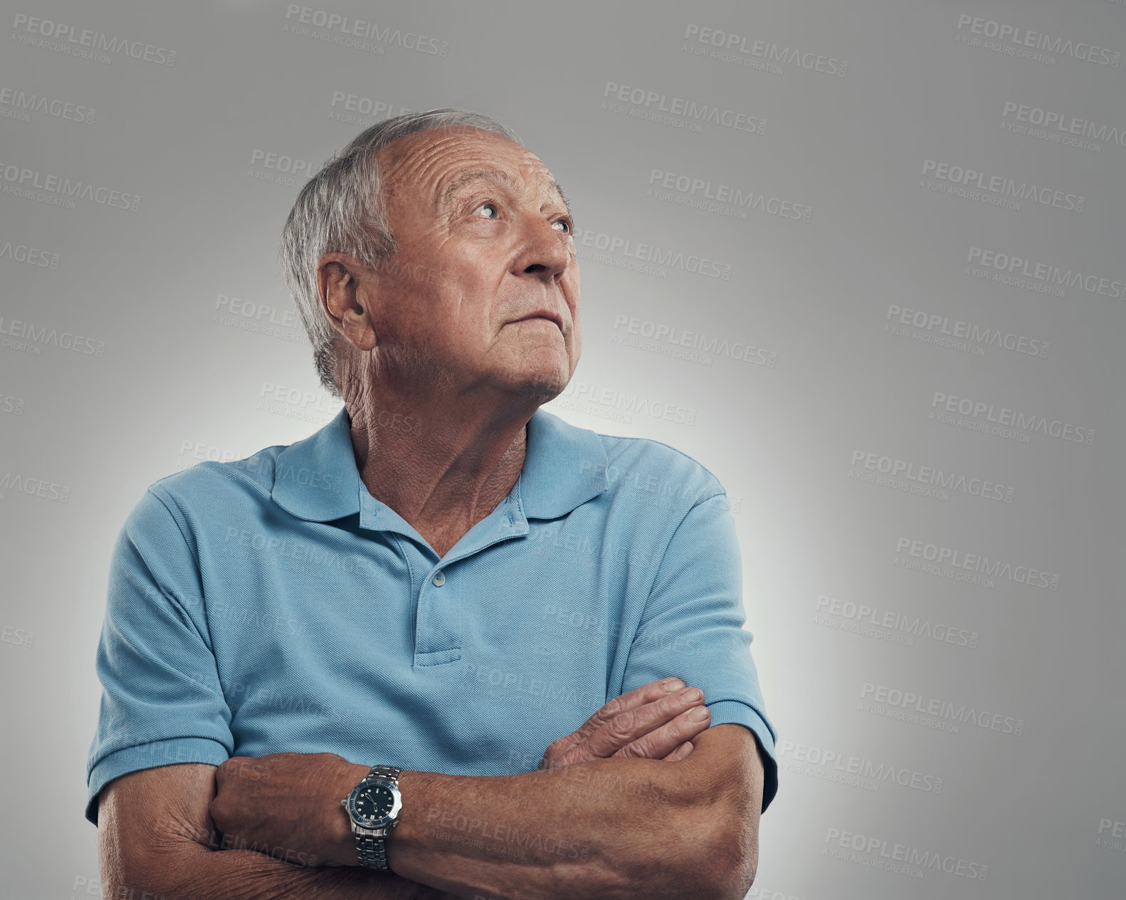 Buy stock photo Shot of an older man with his arms crossed looking off into the distance in a studio against a grey background