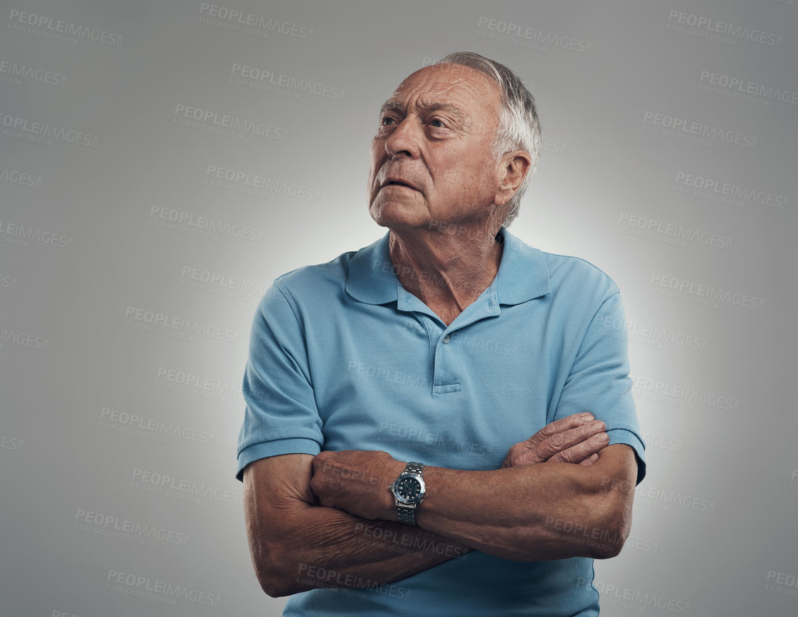 Buy stock photo Shot of an older man with his arms crossed looking off into the distance in a studio against a grey background