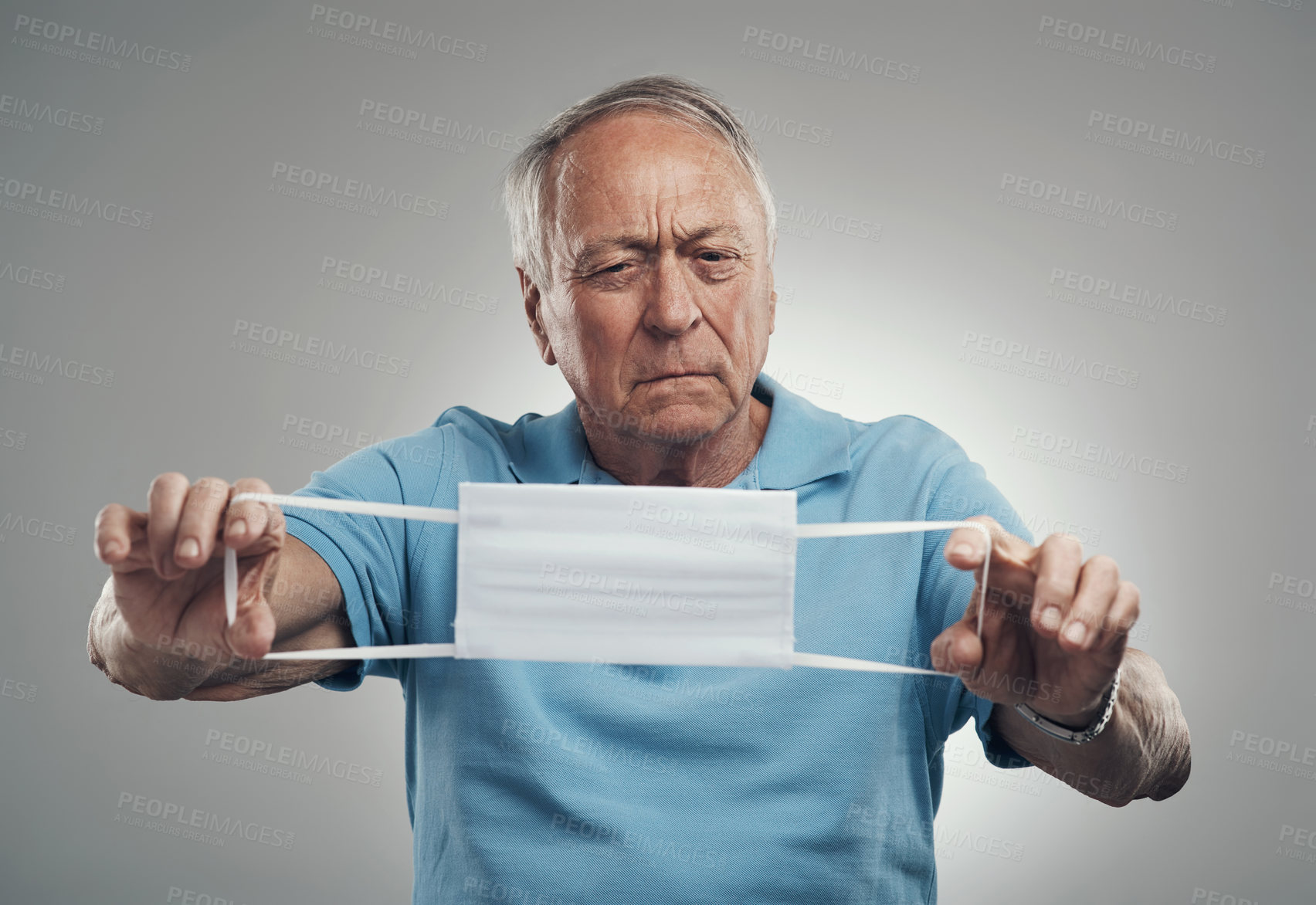 Buy stock photo Shot of an elderly man holding a protective face mask in a studio agains a grey background